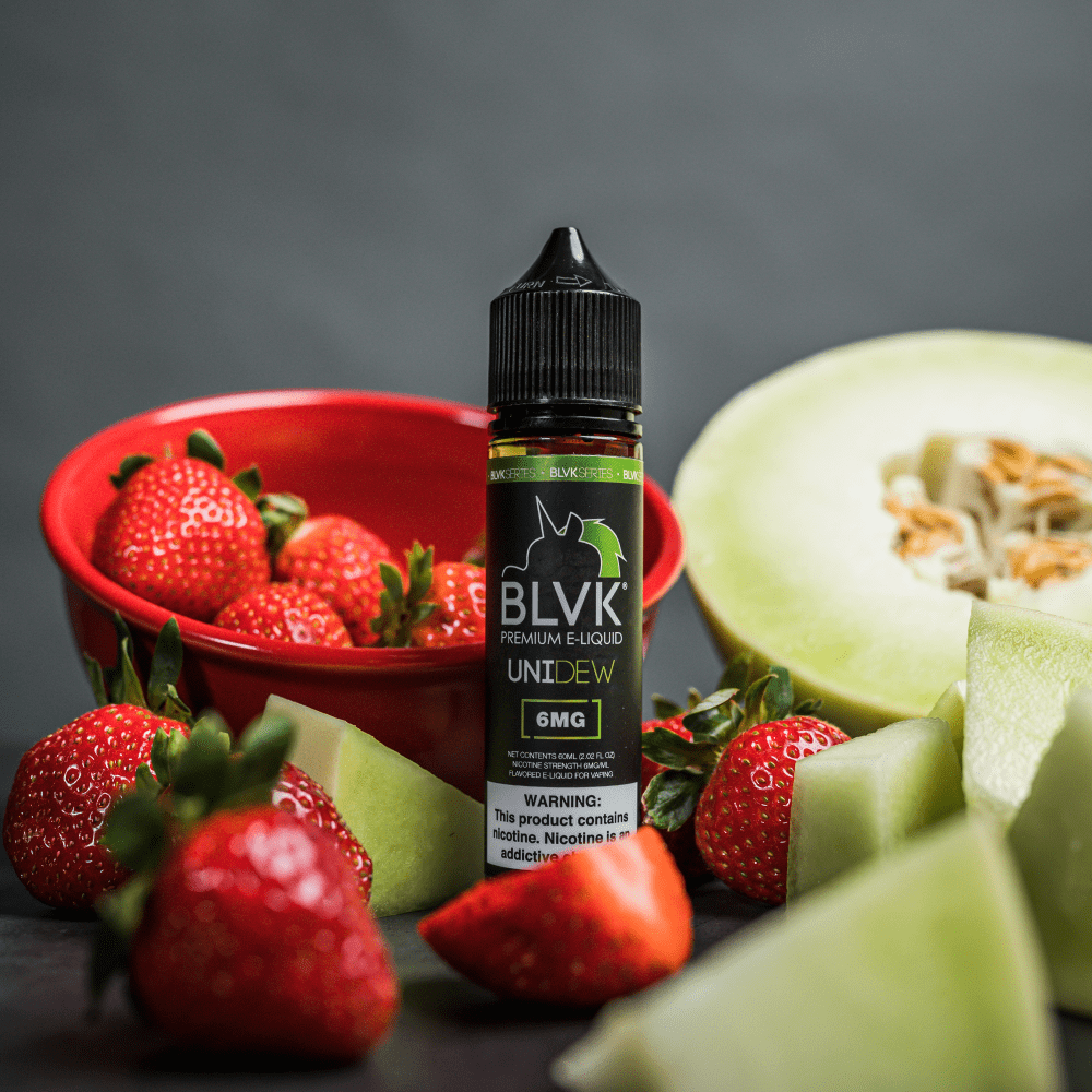 BLVK UNIDEW FREEBASE ELIQUID BOTTLE WITH HONEYDEW AND STRAWBERRIES AROUND IT